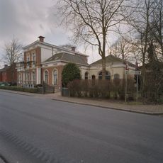Voorm. dienstwoning met blokbepleistering onder schilddak met sierelementen op de hoeken