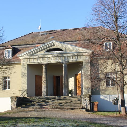 Herrenhaus mit zwei flankierenden Linden vor dem Eingangsbereich, Schornstein der ehemaligen Brennerei , südliche Scheune , südwestliche Einfriedungsmauer des ehemaligen Gartengrundstücks und Reste des Gartens sowie nord