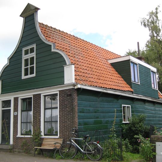 Houten dijkhuis met klokgevel uit de 19de eeuw, bakstenen onderpui in empire stijl