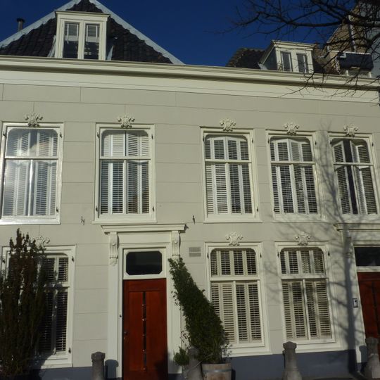 Pand met gepleisterde lijstgevel, deuromlijsting. Stoep met stoeppalen. In de 19e eeuw verfraaid. Zadeldak terzijde eindigend in topgevel