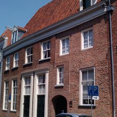 Pand met brede lijstgevel voor oud pand onder hoog dwars schilddak met twee dakkapellen met frontons en hijsbalken