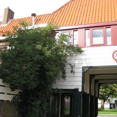Poortgebouw met twee winkels met bovenwoningen, met veel hout zoals de zware kolommen in poort, bouwstijl Amsterdamse School, ligging aan Purmerweg centraal deel van Tuindorp Nieuwendam