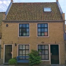 Hoog pand onder zadeldak tegen twee topgevels van gele steen