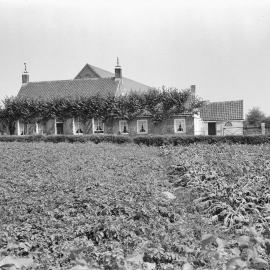 Woonhuis in gele baksteen onder zadeldak en bekroond door hoekschoorstenen met schilden en smeedijzeren siertop. 6-ruits schuiframen