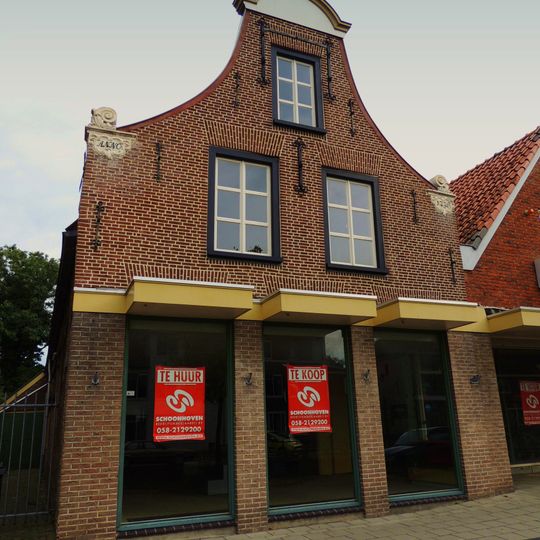 Pand onder zadeldak tegen klokgevel met aanzetkrullen en zesruitsvensters in de top