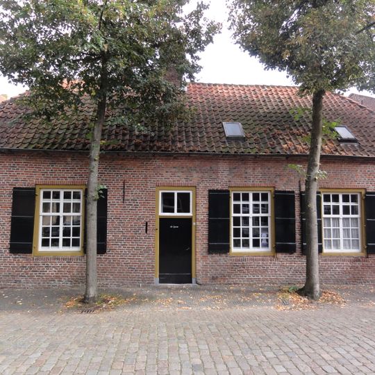 Grijsgepleisterd dorpshuis met dwars wolfsdak van pannen
