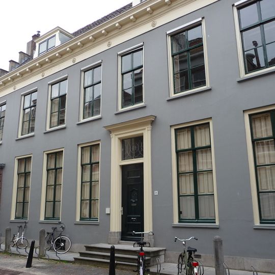 Pand met gepleisterde zeven ramen brede gevel met rechte kroonlijst, zadeldak tussen trapgevels aan de korte zijde