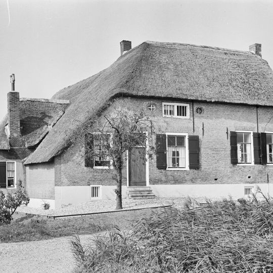 Hoeve onder schilddak met riet gedekt. Voorgevel van gele steen met rode vensterstrekken. Vensters met luiken en zesruitsramen.