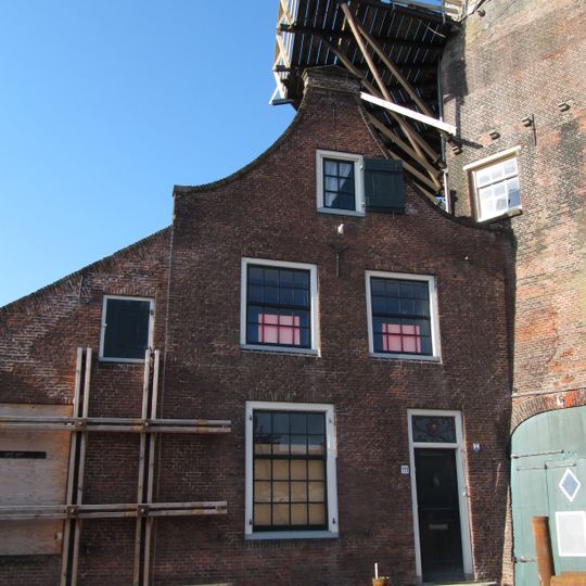 Aan de voet van de molen muldershuis met tuitgevel, verdieping en roedenverdeling uit de bouwtijd. Naast het muldershuis aanbouw onder lessenaarsdak