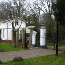 Voormalige diensthuis van de Pauw, gepleisterd. Ernaast hek met hardstenen pijlers door vazen bekroond toegang Pauwhof