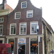 Diep pand onder zadeldak tegen hoge klokgevel met natuurstenen aanzetkrullen en achterhuis van gele steen