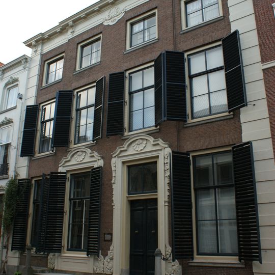 Pand met brede lijstgevel van vier vensterassen, parterre met twee verdiepingen, middenrisaliet en hoekpilasters