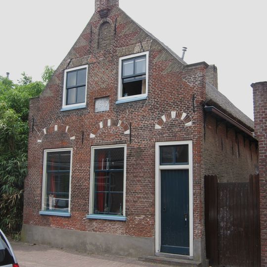 Boerenhuis, bestaande uit begane-grond met zolderverdieping en rieten zadeldak, dat aansluit tegen een puntgevel met geprofileerde zijdekplaten, vlechtingen en toppilaster met gebeeldhouwde bekroning.