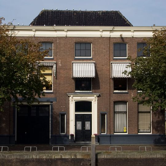 Breed pand met bakstenen gevel op hardstenen sokkel, middenrisaliet, hoekpilasters en kroonlijst met consoles