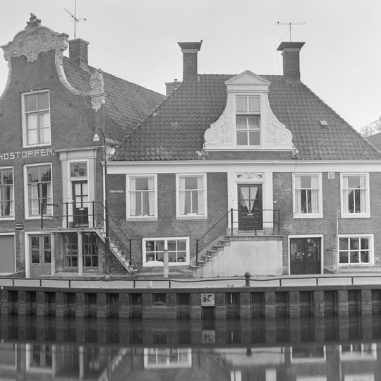 Breed pand met hoge kelderverdieping en bordes onder hoog schilddak met dakkapel en twee hoekschoorstenen met borden