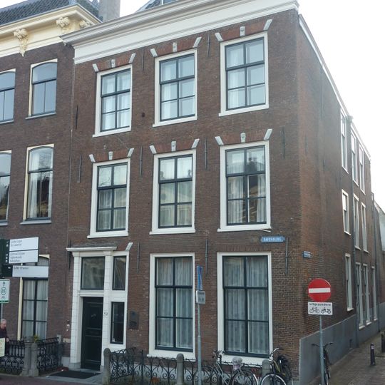 Pand met gewijzigde trapgevel door rechte kroonlijst afgedekt. Goede voordeur met knop. Boven vensters maskersluitstenen