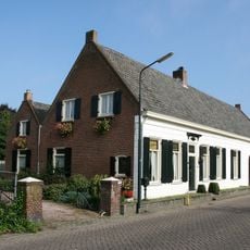 Boerderij van het langgeveltype. Woonhuis en stal onder een pannen zadeldak tussen puntgevels. Lagere aanbouw onder zadeldak tegen de achtergevel.