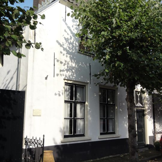 Gepleisterd pand onder pannen wolfdak, met in de voorgevel beneden zesruitsschuiframen. IJzeren stoephekjes