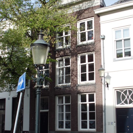 Huis met eenvoudige gevel met rechte kroonlijst met tympaan. Gebeeldhouwde deur. Levensboom in bovenlicht