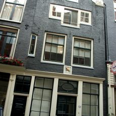 Huis met gevel die in de top van de klokvormige bekroning met rollagen een oude gevelsteen bevat