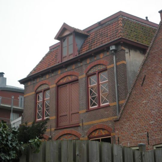 Pakhuis van twee bouwlagen onder een afgeplat schilddak gedekt met rode kruispannen