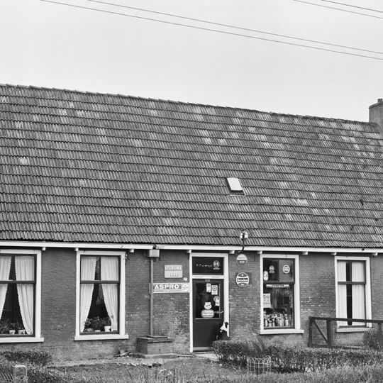 Dubbel pand met bakgoot op klossen onder zadeldak evenwijdig aan de straat tussen twee topgevels