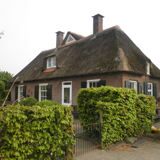 Boerderij De Riete-Rietman met dwars geplaatst woonhuis opgetrokken in rode machinale baksteen onder rietgedekt schilddak, het bedrijfsgedeelte onder rietgedekt wolfsdak met uilenbord