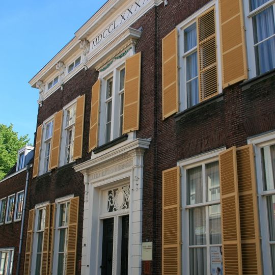 Fors pand met bakstenen gevel op smalle natuurstenen plint. Twee traveeën aan elke zijde van de risalerende middenpartij