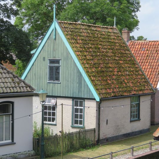 Pand met gepleisterde muren; zadeldak met nok evenwijdig aan de rooilijn. Houten zijgeveltopbeschietingen