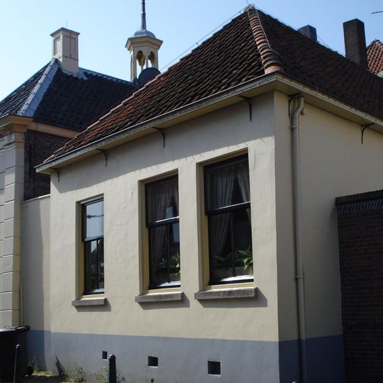 Gepleisterd pand zonder verdieping, met pannen schilddak, achter het voormalige raadhuis