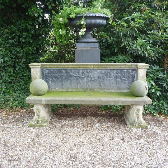 Twickel: gietijzeren tuinvaas achter de tuinbank in de oranjerietuin in schaalvorm op sokkel van beton