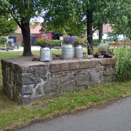 Dorfanger mit Wiese, Baumreihen, Solitärbäumen und der Friedenseiche mit Gedenktafel aus Anlass des 25-jährigen Jubiläums des Deutsch-Französischen Krieges, dazu die Milchrampe und die Steindeckerbrücke der verlängerten Posottendorfer Straße