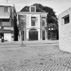 Poortgebouw van twee bouwlagen hoog, drie traveeën breed en gedekt door een met pannen belegd T-vormig schilddak