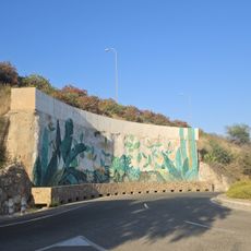 El mural representa sobre fondo blanco un paisaje vegetal, con hojas de helechos, plantas trepadoras, flores amarillas y una mariposa.