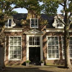 Vrijstaand breed laag woonhuis, met ingezwenkte en door fronton gedekte middentop voor dwarskap