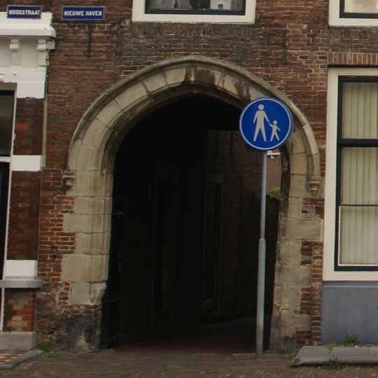 Doorgang met brede gotische poortomlijsting, afgesloten door smeedijzeren hek, overbouwd door het pand Nieuwe Haven 1