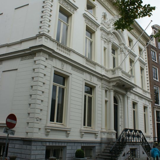 Dubbel hoekpand, gebouwd in 1685, geheel verbouwd in 1860/61 door cornelis outshoorn, met van rijke stucversieringen voorziene gepleisterde gevels onder bewerkte lijst, en zandstenen pui met balcon