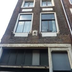 Pand met fragment van Dorische pilastergevel door kroonlijst afgedekt. Vlakke gevelstenen met jaartal en leeuwenmasker, pui vernieuwd