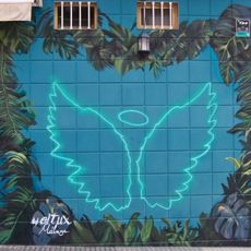 Mural con una alas y un aro luminosos simulado los atributos de un ángel, enmarcados entre elementos vegetales. El mural funciona como espacio para tomarse fotos, a modo de fotocol.