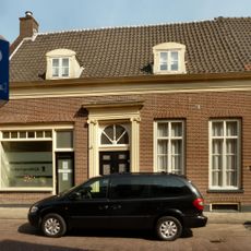 Linker gedeelte van een woonhuis van begane-grond met hoog, dwars zadeldak tussen puntgevels