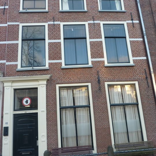 Pand met bakstenen gevel met rechte kroonlijst, deuromlijsting Lod. XV op metselwerk van verdieping resten van geverfde banden. Hardstenen stoep met palen