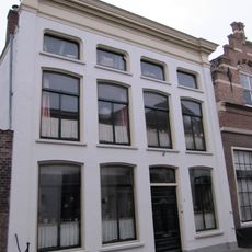 Pand, bestaande uit twee huizen onder schilddaken, in het derde kwart 19e eeuw samengetrokken achter een gepleisterde lijstgevel ter breedte van vier vensterassen