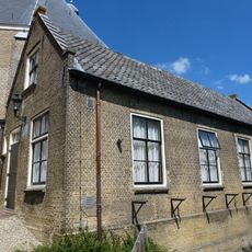 Tegen de z.o.zijde van het koor een huisje met zadeldak en puntgevel met rollaag, gedateerd in een steen