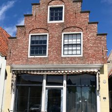 Pand onder zadeldak tegen gepleisterde trapgevel met verhoogd achterhuis tussen twee puntgevels