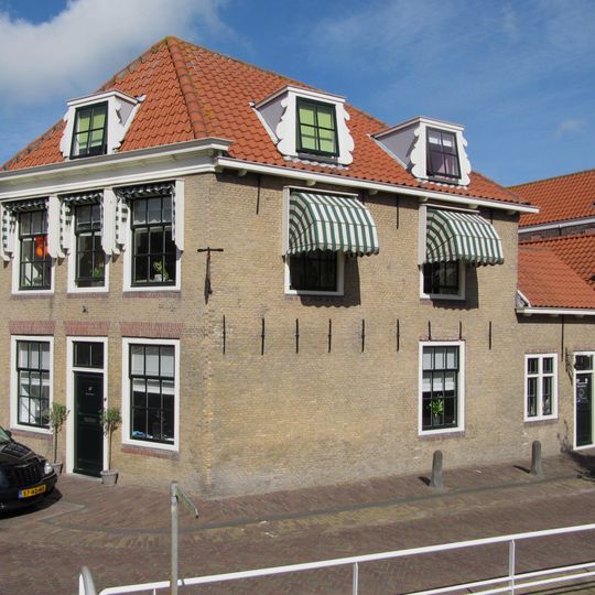 Hoekpand met hoog schilddak, lijstgevel en achterbouw met oude kozijnen en luiken