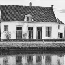 Lage witgepleisterde hofstede met uitbouw, zadeldak in topgevels eindigend