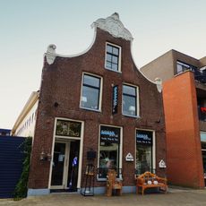 Pand onder zadeldak tegen klokgevel met gebeeldhouwde aanzetkrullen en bekroning