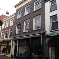 Pand met rechte kroonlijst, onder zadeldak. Beneden verbouwd