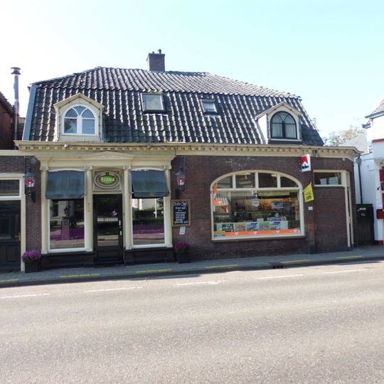Verdiepingloos pand onder mansarde dak; daterend uit de bouwtijd van de kerk en in een verband daarmee aangelegd