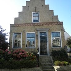 Vrij diep pand onder zadeldak tussen topgevels waarvan de versierde voorgevel trapvormig is